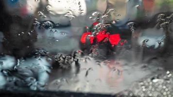 sfocatura dello sfondo astratto dal parabrezza di un'auto nel guardare attraverso molte gocce di pioggia fino alla luce rossa alla fine dell'auto, che era parcheggiata in strada di notte. foto