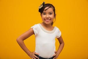 bella ragazza asiatica seduta su sfondo giallo. felice piccola ragazza asiatica sorridente. foto
