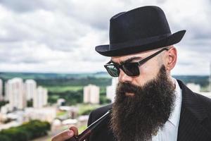 elegante uomo barbuto che fuma la pipa guardando l'orizzonte dalla cima di un edificio alto. foto