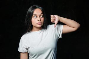 adolescente bruna infelice non è d'accordo facendo un segno di gesto pollice in giù. ragazza che mostra disapprovazione mentre mostra il pollice in giù. foto