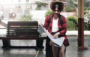 viaggio, ritratto di una ragazza asiatica carina che guarda una mappa per pianificare un viaggio mentre aspetta alla stazione ferroviaria foto