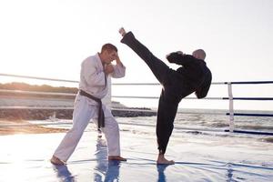 combattenti di karate stanno combattendo sul ring di pugilato della spiaggia al mattino foto