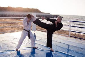 combattenti di karate stanno combattendo sul ring di pugilato della spiaggia al mattino foto