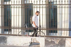 giovane uomo barbuto con zaino in pelle che cammina con la bicicletta nera foto