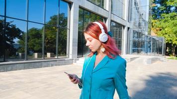 giovane donna con abito colorato e capelli rosa beve caffè e ascolta musica nel parco foto