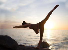 fitness razza mista donna asiatica in posa yoga sulla spiaggia del mattino, bella donna in forma pratica fitness exrxise pietre, mare mattutino o sfondo oceano foto