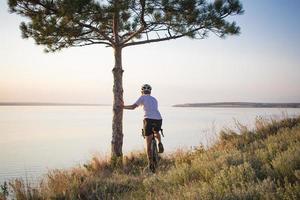 ciclista su ciclocross professionale in bicicletta in discesa, pino e sfondo del lago foto