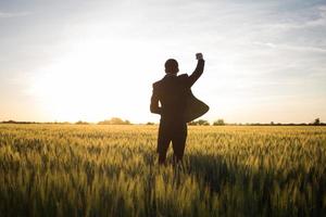 concetto di vincitore, felice giovane imprenditore salta con le mani alzate nei campi, piante di grano estivo foto