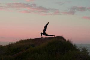 donna in forma che fa esercizio di stretching yoga all'aperto nel bellissimo paesaggio delle montagne. femmina sulla roccia con mare e alba o tramonto formazione di sfondo asans. sagoma di donna in pose yoga