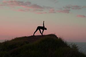 donna in forma che fa esercizio di stretching yoga all'aperto nel bellissimo paesaggio delle montagne. femmina sulla roccia con mare e alba o tramonto formazione di sfondo asans. sagoma di donna in pose yoga foto