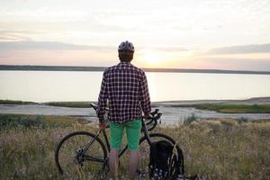 silhouette di un uomo con bici da strada da turismo che guarda e fa foto del tramonto nel lago sul cellulare