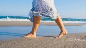 giovane bella donna vestita con un abito bianco cammina a piedi nudi sulla spiaggia estiva foto