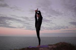 donna in forma che fa esercizio di stretching yoga all'aperto nel bellissimo paesaggio delle montagne. femmina sulla roccia con mare e alba o tramonto formazione di sfondo asans. sagoma di donna in pose yoga