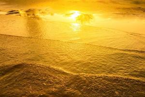 luce dorata che si riflette su un'onda d'acqua al mare e sabbia sul tramonto. tono oro puro foto