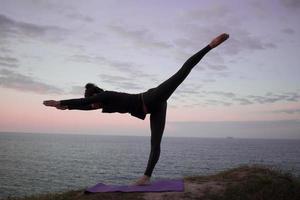 donna in forma che fa esercizio di stretching yoga all'aperto nel bellissimo paesaggio delle montagne. femmina sulla roccia con mare e alba o tramonto formazione di sfondo asans. sagoma di donna in pose yoga foto