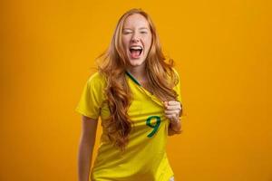 sostenitore del Brasile. fan della donna rossa brasiliana che celebra il calcio, partita di calcio su sfondo giallo. colori brasiliani. foto