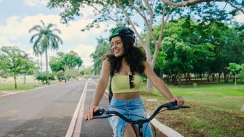 la giovane donna latina con il casco protettivo sta andando in bicicletta lungo la pista ciclabile in un parco cittadino foto