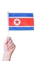 la mano tiene la bandiera del paese della dprk su uno sfondo bianco isolato. foto