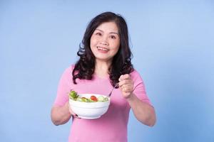 immagine della donna asiatica di mezza età che mangia insalata su sfondo blu foto