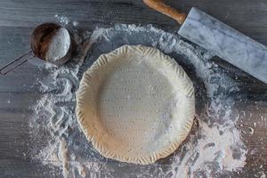 fare una torta rustica di pasta frolla su una superficie infarinata con un mattarello piatto foto