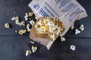 popcorn del sacchetto aperto strappato e che si rovescia su una superficie piatta foto