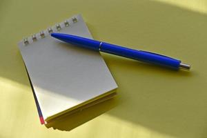 penna stilografica blu e blocco note su sfondo giallo foto