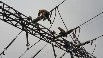 due elettricisti stanno effettuando riparazioni e manutenzione sulla torre elettrica foto