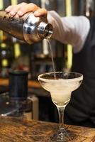 barman al lavoro, preparare cocktail. versando la margarita nel bicchiere da cocktail.