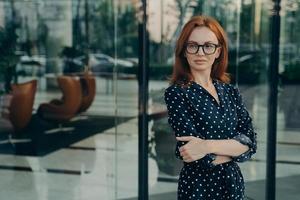 La regista femminile sicura di sé con i capelli rossi posa vicino all'edificio per uffici foto