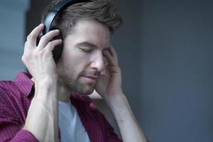 giovane uomo tedesco soddisfatto con gli occhi chiusi che ascolta musica in cuffia a casa con la faccia felice foto