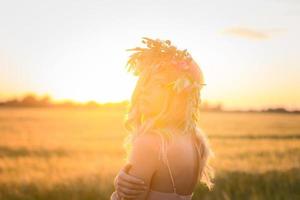 ritratti di giovane donna che si diverte nel campo di grano durante il tramonto, signora in testa corona di fiori durante foto