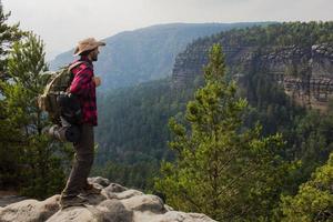 giovane escursionista maschio stare sulla scogliera in montagna con baclpack e cappello foto