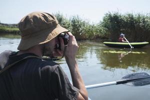 il giovane viaggiatore maschio con la macchina fotografica nuota sul kayak nel fiume foto