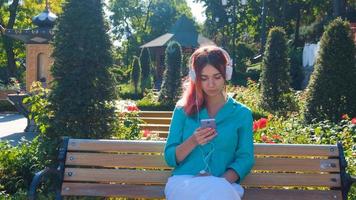 giovane donna con abito colorato e capelli rosa beve caffè e ascolta musica nel parco foto