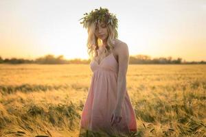 ritratti di giovane donna che si diverte nel campo di grano durante il tramonto, signora in testa corona di fiori durante foto