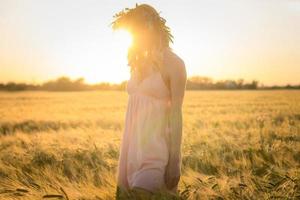 ritratti di giovane donna che si diverte nel campo di grano durante il tramonto, signora in testa corona di fiori durante foto