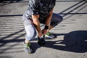 giovane atleta maschio barbuto che si allena nella zona industriale in una giornata di sole, esercizi di kettlebell all'aperto, fondo urbano foto