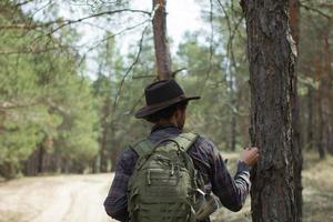 vista posteriore di giovane escursionista maschio in cappello da cowboy che cammina all'aperto in una giornata estiva. viaggiatore hipster. foto