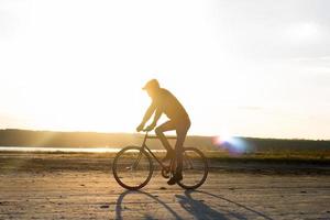 pilota da solo su bici da strada a scatto fisso che guida nel deserto vicino al fiume, foto di ciclista turistico hipster.