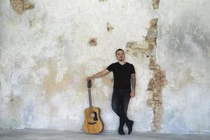 giovane maschio con la chitarra nella stanza vuota, musicista e cantautore da solo in studio foto