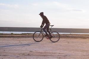 pilota da solo su bici da strada a scatto fisso che guida nel deserto vicino al fiume, foto di ciclista turistico hipster.