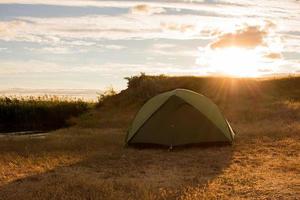 tenda verde di escursionisti vicino al fiume durante il tramonto o l'alba foto
