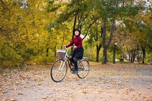 giovane donna nel parco autunnale leggere il libro, bella femmina rossa con la bicicletta sull'erba verde foto