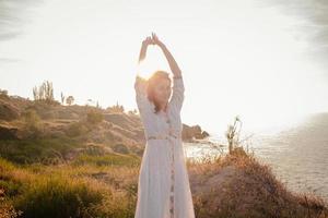 giovane donna che cammina sulla spiaggia del mattino in un bellissimo vestito bianco. femmina adatta che si diverte durante la tura dell'alba. foto