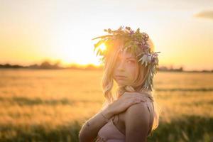 ritratti di giovane donna che si diverte nel campo di grano durante il tramonto, signora in testa corona di fiori durante foto