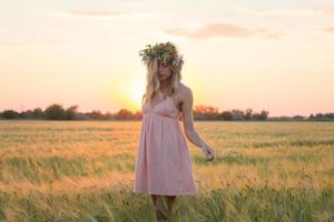 ritratti di giovane donna che si diverte nel campo di grano durante il tramonto, signora in testa corona di fiori durante foto