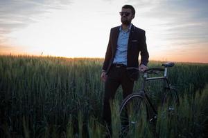 un uomo d'affari caucasico in sella a una bicicletta nei campi estivi, maschio in giacca e cravatta su una bici fissa. foto