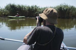 il giovane viaggiatore maschio con la macchina fotografica nuota sul kayak nel fiume foto