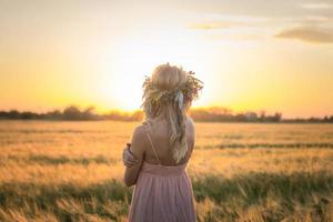 ritratti di giovane donna che si diverte nel campo di grano durante il tramonto, signora in testa corona di fiori durante foto