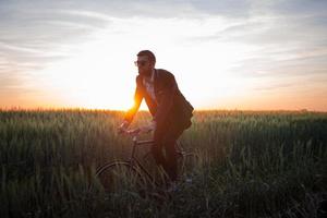 un uomo d'affari caucasico in sella a una bicicletta nei campi estivi, maschio in giacca e cravatta su una bici fissa. foto